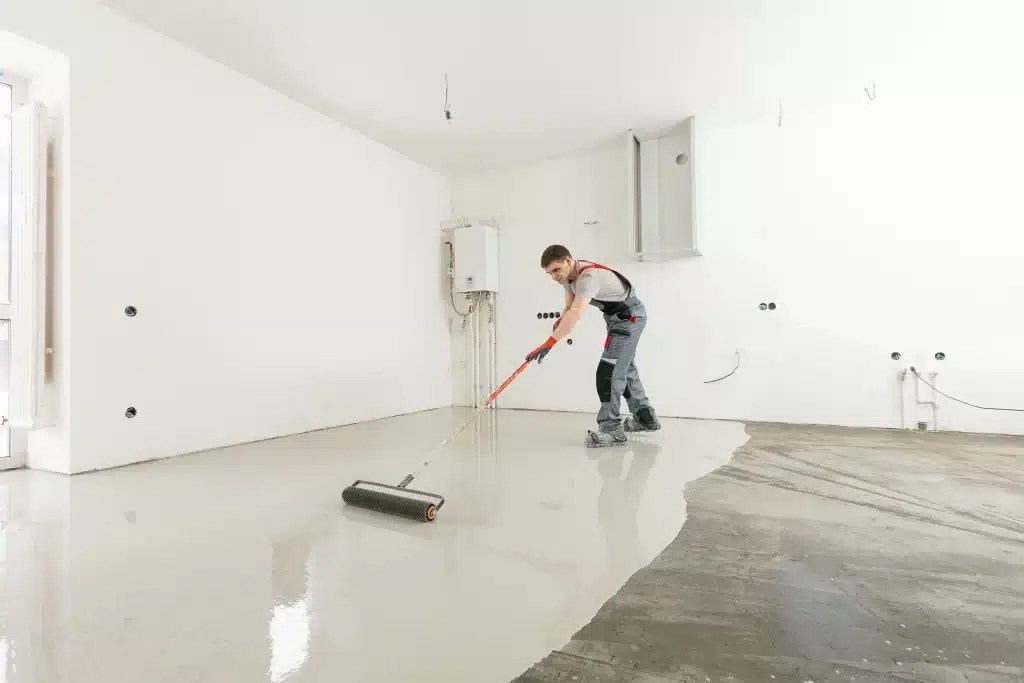 Worker leveling concrete floor in unfinished room.